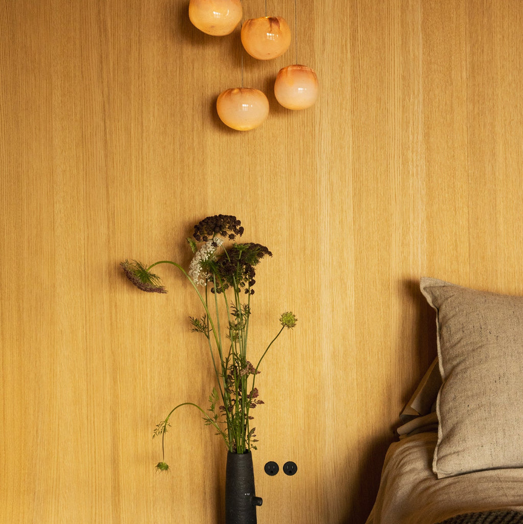 Decorative wall with hanging lights, a vase of flowers, and minimal Bocci Flush Outlets beside a bed on a wood wall. 