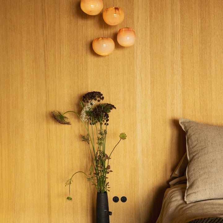 Decorative wall with hanging lights, a vase of flowers, and minimal Bocci Flush Outlets beside a bed on a wood wall. 