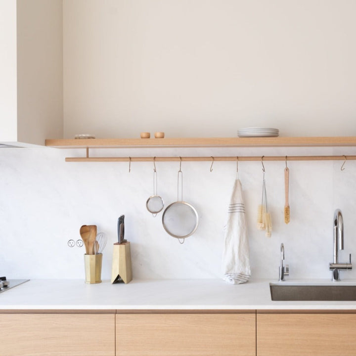 Bocci 22 white flush outlets installed in a white marble stone backsplash within a Nordic-style kitchen featuring oak cabinets, wood shelf, and hanging rod with minimal Japanese kitchen tools. Oji Masanori brass utensil and knife holder on countertop.