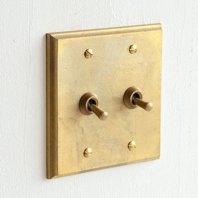 A Multi Square brass switch plate mounted to a white wall by MATUREWARE.
