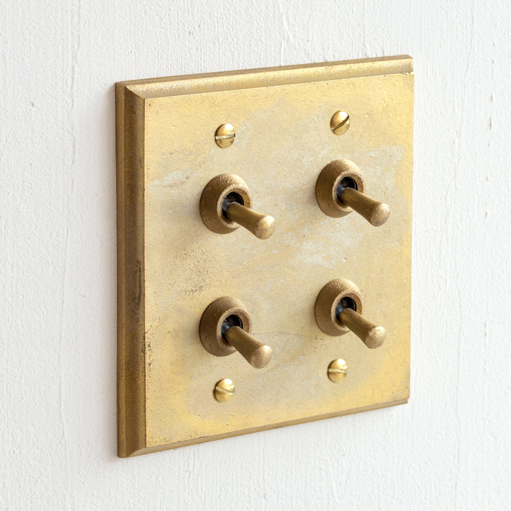 A MATUREWARE Brass Switch Plate - Multi Square with four knobs on a white wall.