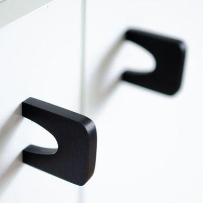 A close up of two Bridge Knobs in black from Baccman Berglund on a white cabinet.