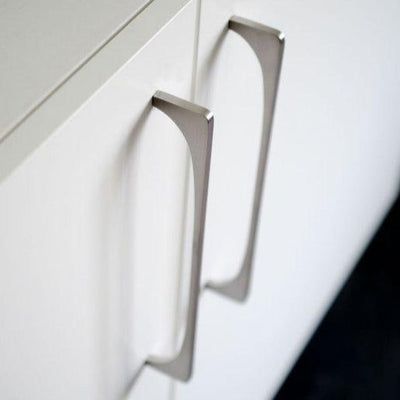 A close up of two Baccman Berglund Bridge Pull handles on a white cabinet.