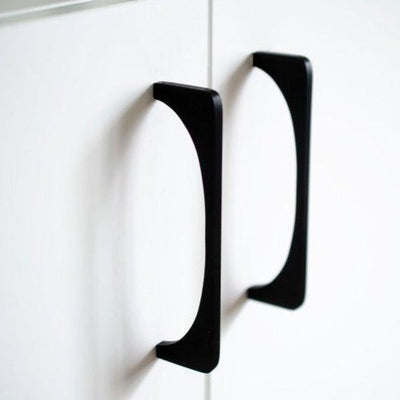 A pair of Baccman Berglund Bridge Pull handles on a white cabinet.