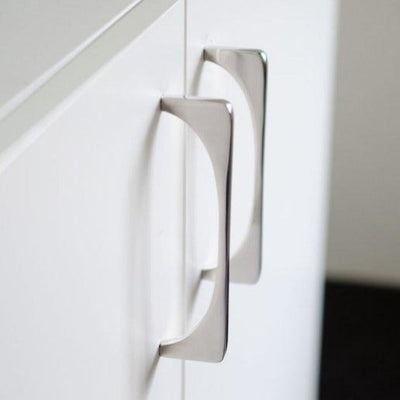 A close up of a Baccman Berglund Bridge Pull on a white cabinet.