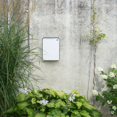 a Serafini Cap Mailbox on a wall next to some plants.