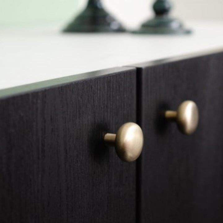 Close-up of dark wooden cabinet with soft mid century brass knobs
