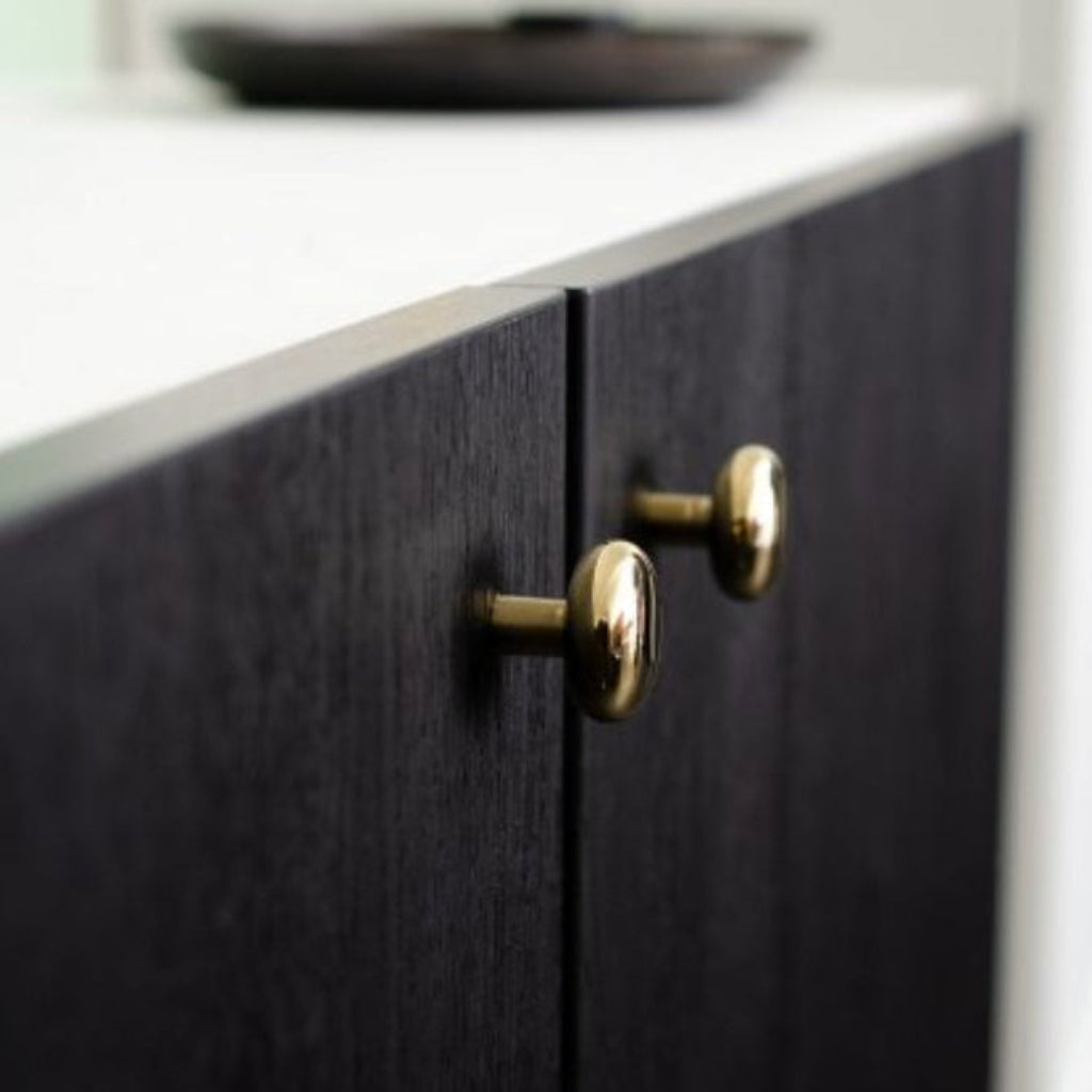 Close-up of a dark wooden cabinet with brass knobs on a light-colored countertop.