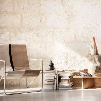A Ferm Living Cashmere Soil Desert Lounge Chair sitting next to a stack of books.