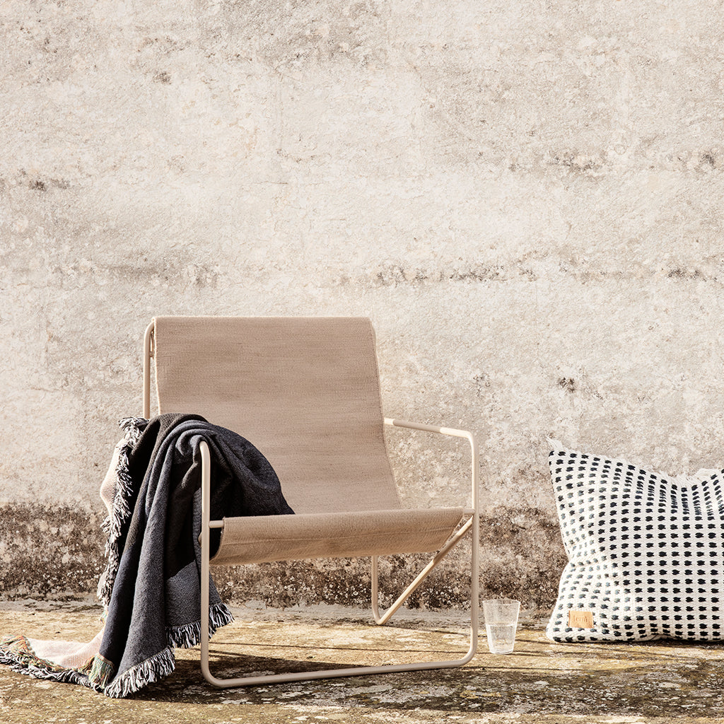 A Ferm Living Cashmere Solid Desert Lounge Chair and a pillow on the ground.