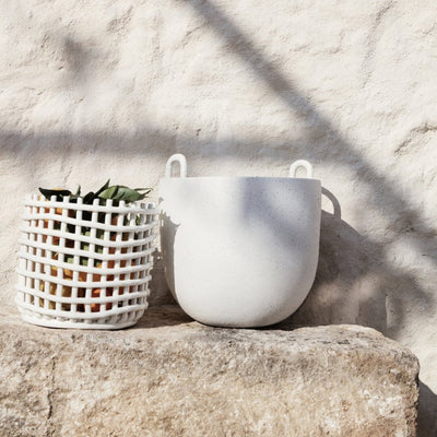 A Ferm Living Ceramic Woven Basket sitting on top of a stone wall.