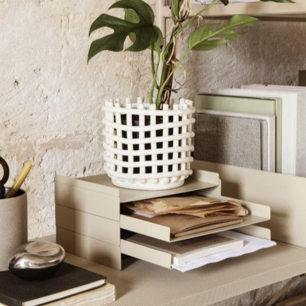 a desk with a Ferm Living Ceramic Woven Basket containing a potted plant on top of it.