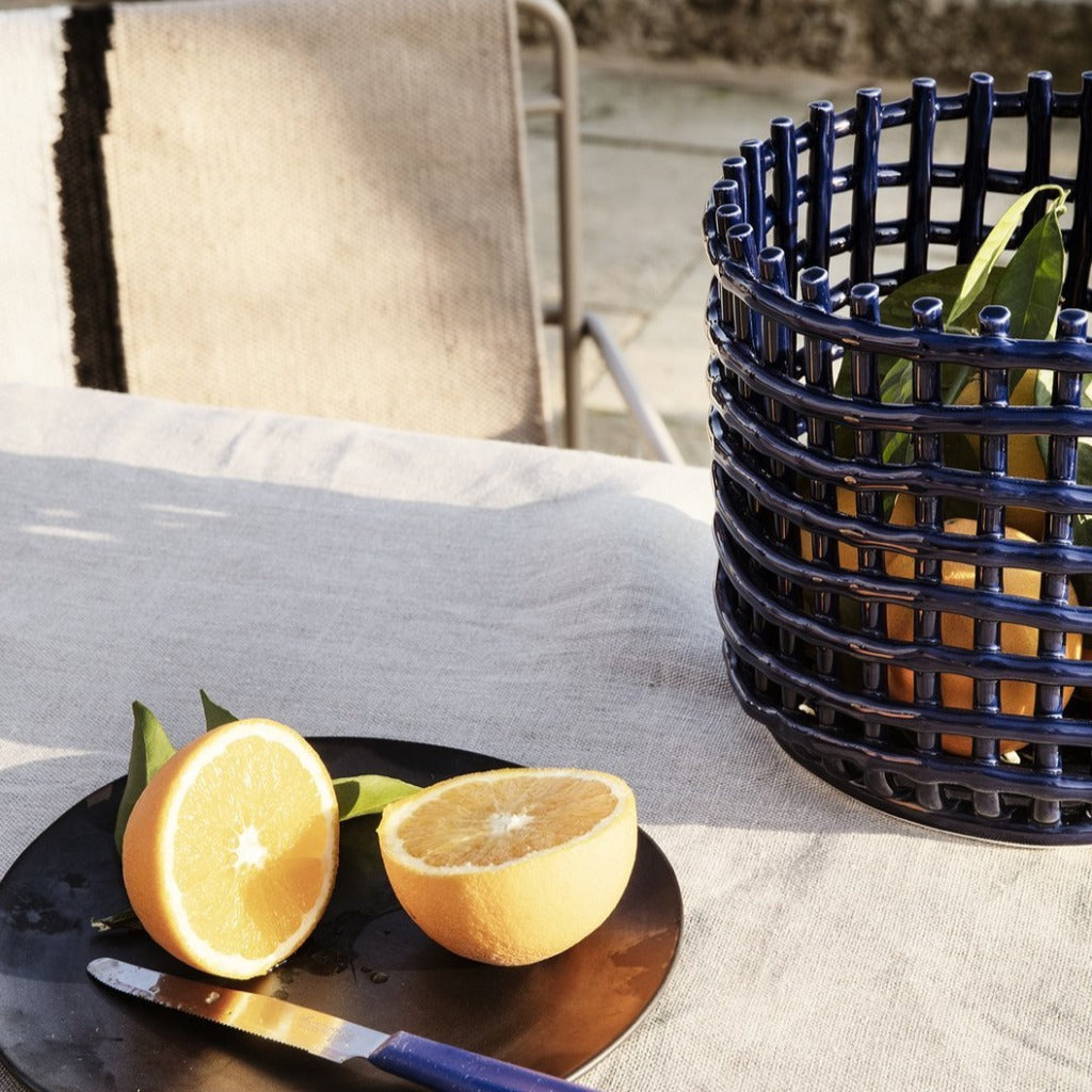 A Ceramic Woven Basket by Ferm Living filled with sliced oranges sitting on a table.