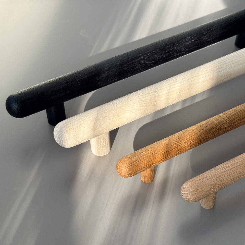 Chapman & Bose wood bar pulls in black, white and oak on a tan wall.