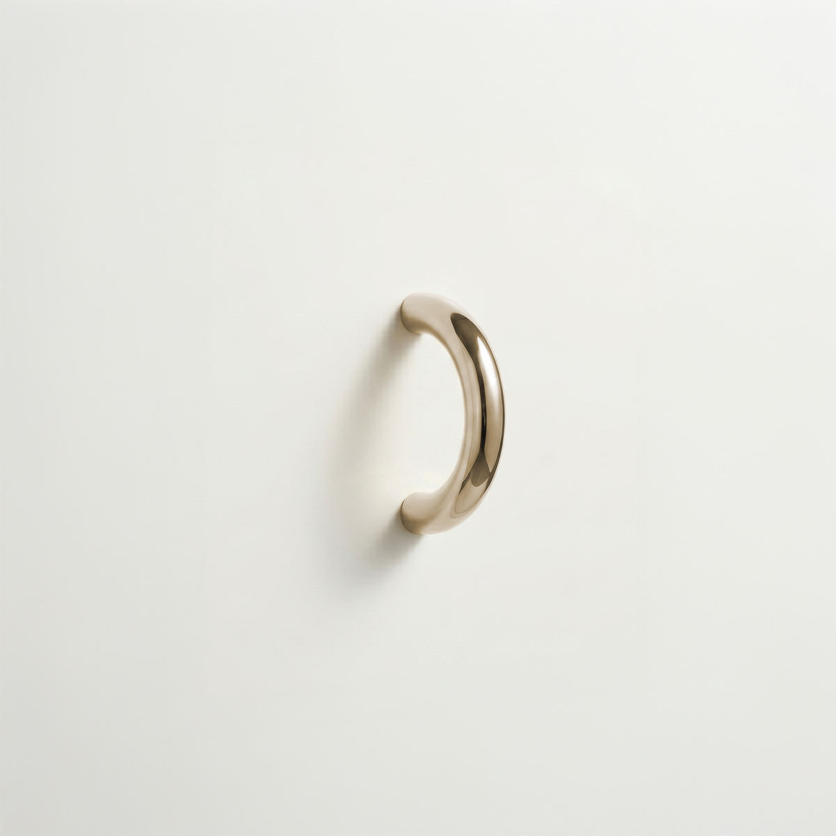 Polished brass Charlie Arc pull, a small half-round arc handle, mounted on a white surface.