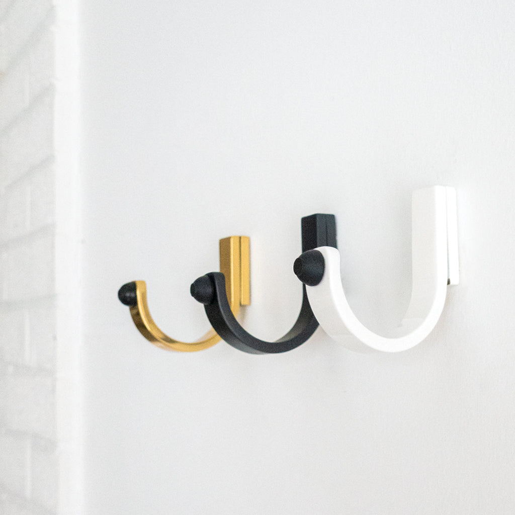 A couple of CBH Charlie Bumper Hooks in black and gold on a white wall.