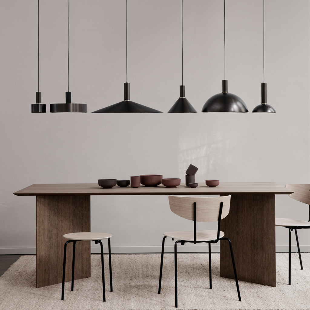 A dining room table with Ferm Living's Collect Angle Shade lights hanging above it and chairs.