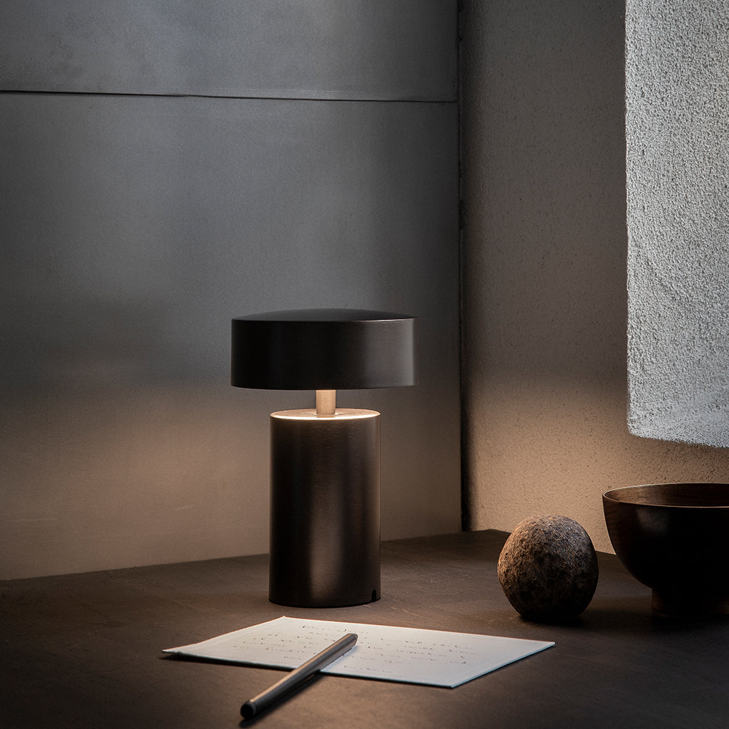 A table with an Audo Column LED Table Lamp and a notepad on it.