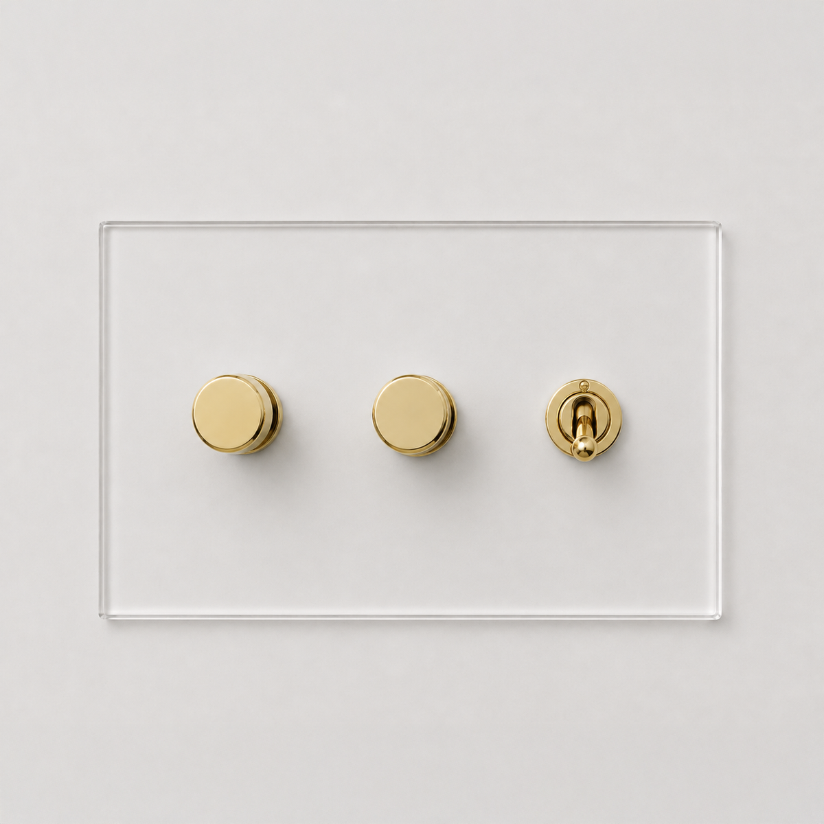 Forbes & Lomax invisible acrylic wall plate with two gold rotary dimmers and one gold toggle switch on a white background.
