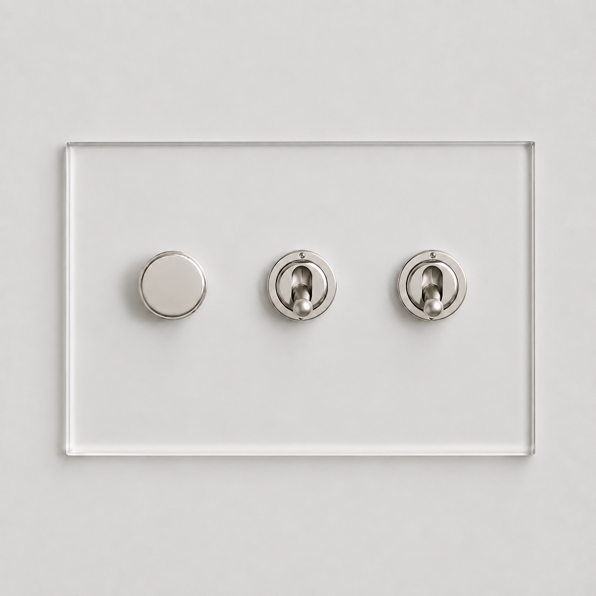 Forbes & Lomax invisible acrylic plate with one nickel rotary dimmer and two nickel toggle switches on a white wall.
