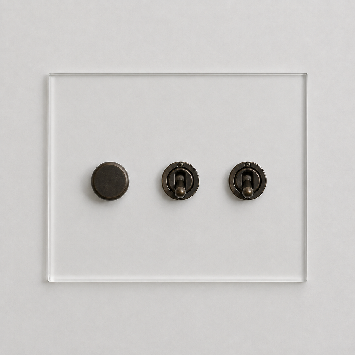 Forbes & Lomax invisible acrylic plate with one rotary dimmer and two bronze toggle switches on a white wall.