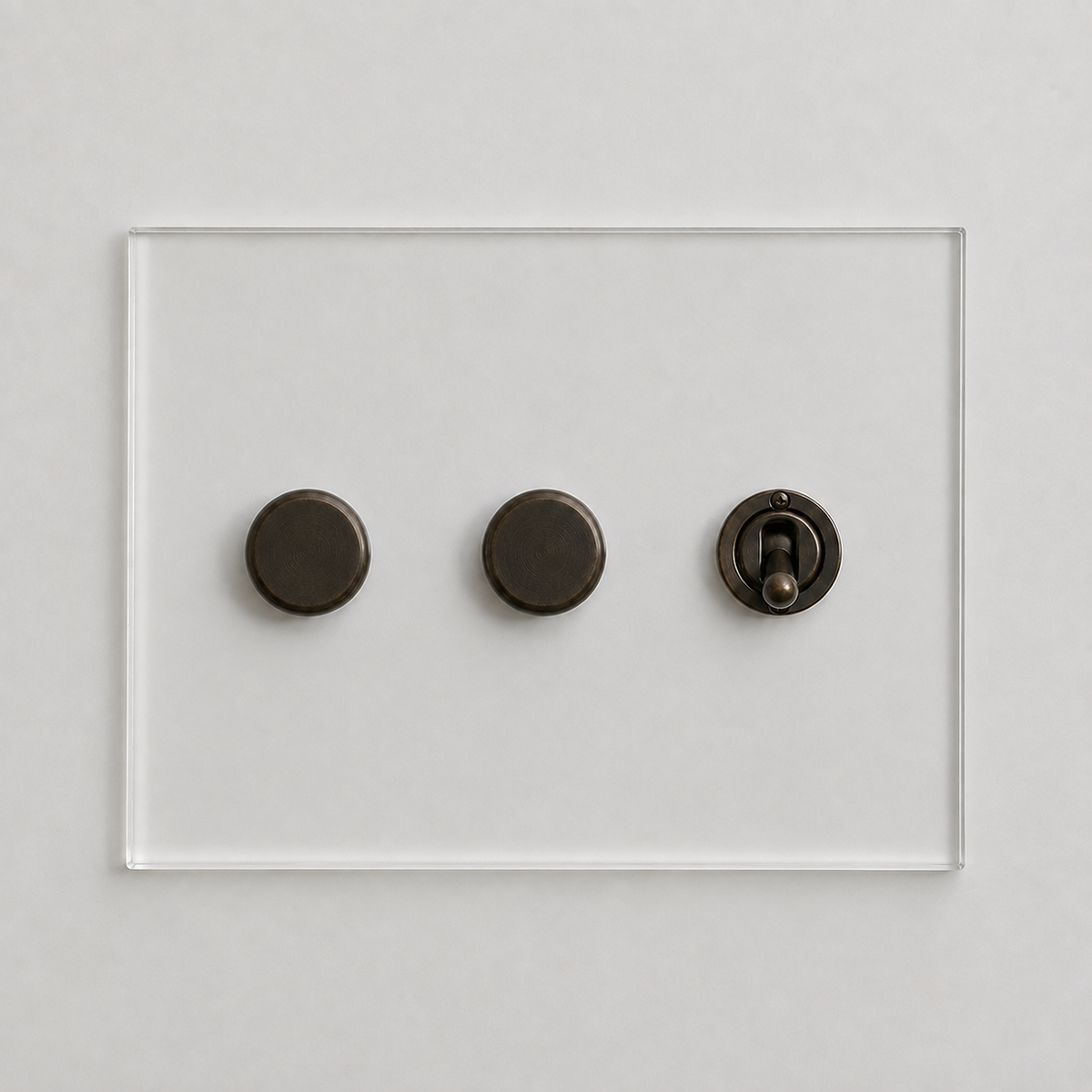 Forbes & Lomax transparent acrylic plate with two bronze rotary dimmers and one bronze toggle switch on a white wall.