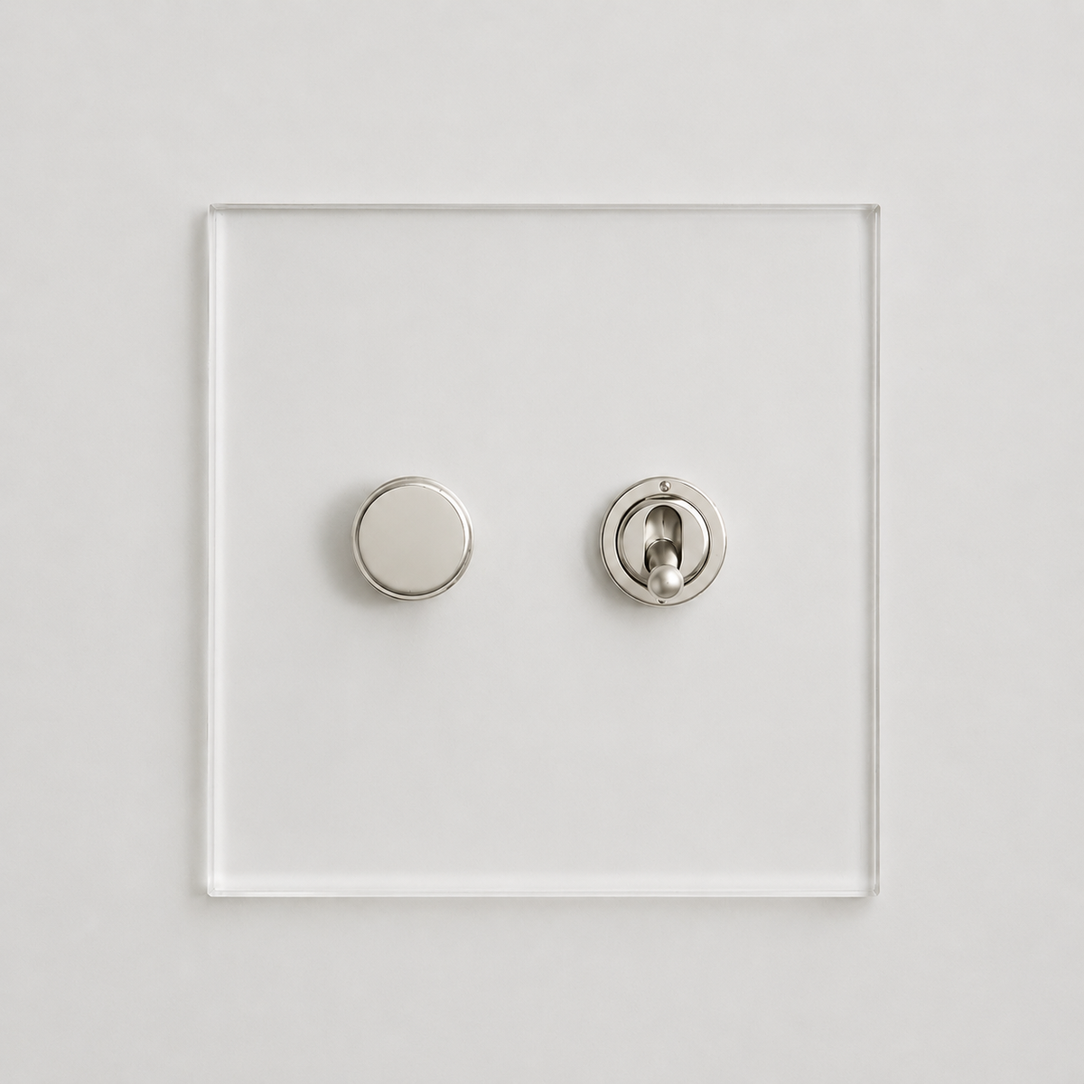 A minimalist modern wall switch plate featuring a square clear acrylic panel with two circular controls in a brushed silver finish, set against a clean white background.