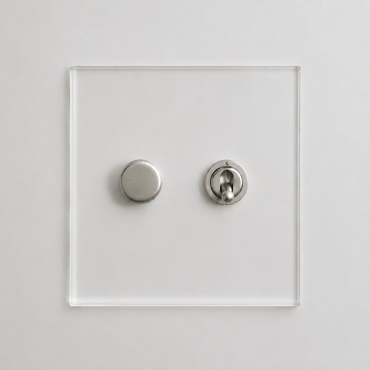 A minimalist modern wall switch plate made of clear acrylic with two round silver metal controls, shown against a clean white background.