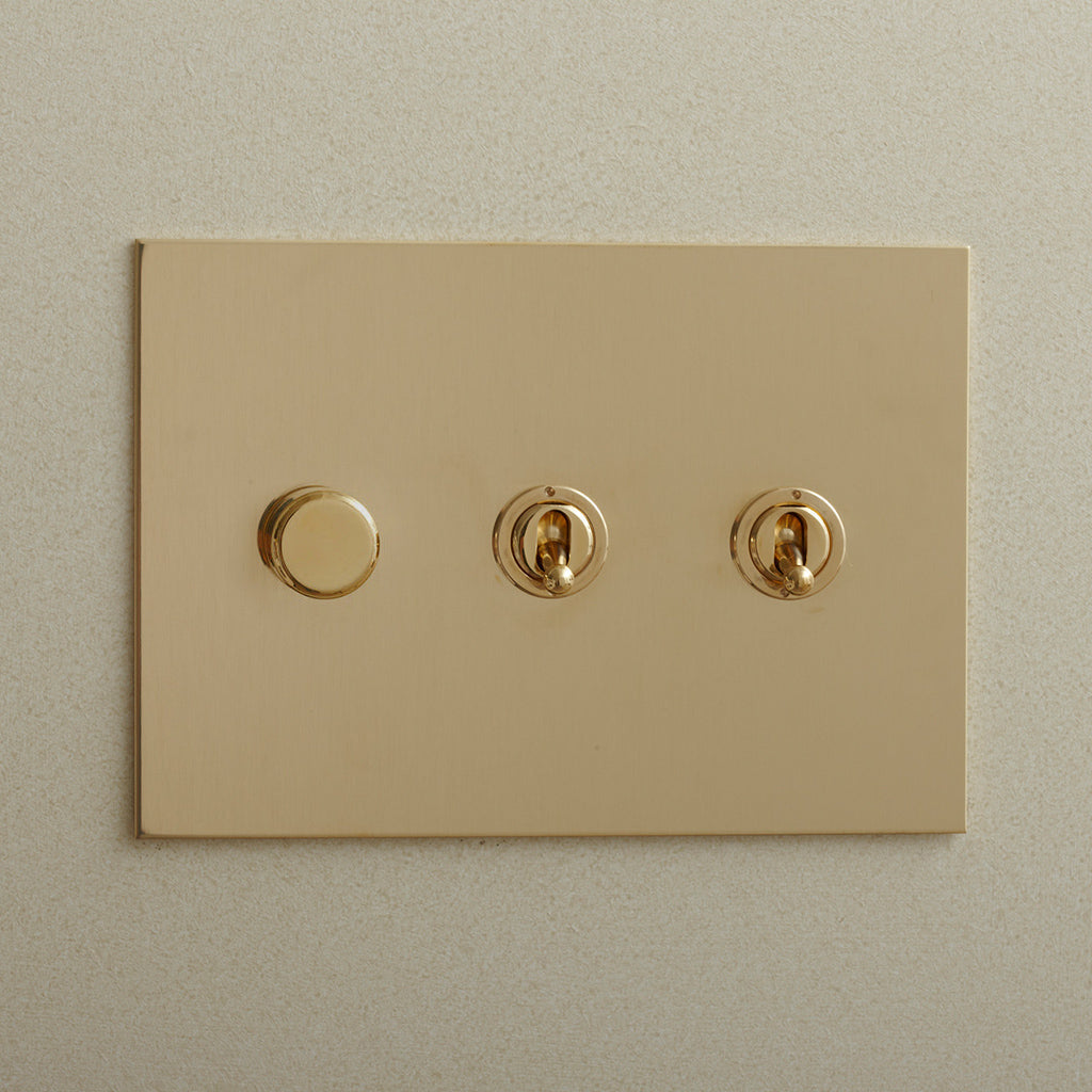 Brass Forbes & Lomax switch plate with a dimmer and two toggles.