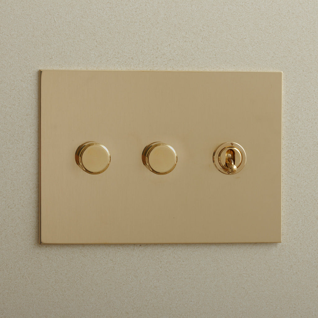 Brass Forbes & Lomax switch plate with two dimmers and a toggle.