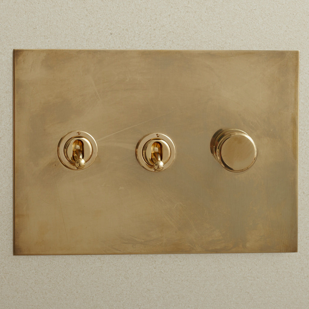 Aged brass Forbes & Lomax switch plate with two toggles and a dimmer.
