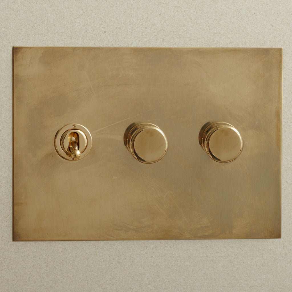 Aged brass Forbes & Lomax switch plate with a toggle and two dimmers.