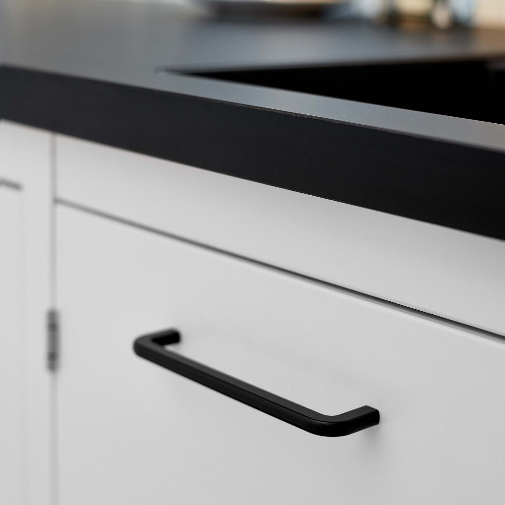 Matte black Furnipart Compact cabinet handle, 160 mm, on a white drawer under a black countertop.