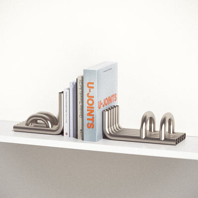 stainless steel TUBE Bookends photographed on a white shelf with a collection of books in between on a white background