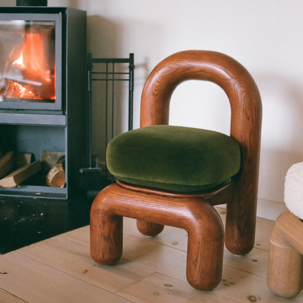 lithic dining chair in red oak and green velvet upholstery on wooden floor beside fire place