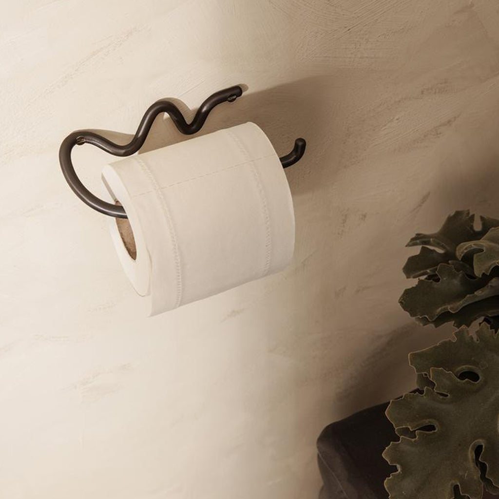 A Ferm Living Curvature Toilet Roll Holder hanging on a wall.