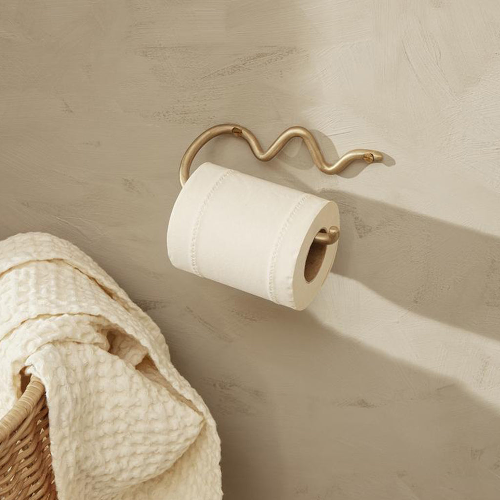 A Curvature Toilet Roll Holder by Ferm Living hanging on a wall next to a towel.