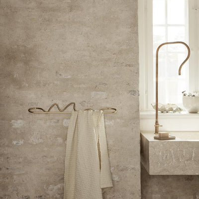 A Ferm Living Curvature Towel Bar hanging on a rack in a bathroom.