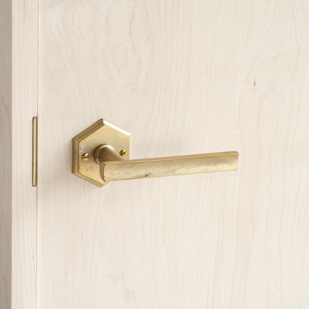 A close up of a MATUREWARE Curved Lever door handle on a wooden door.