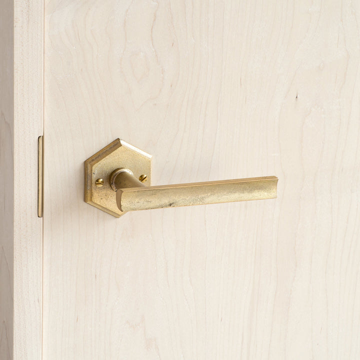 A close up of a MATUREWARE Curved Lever door handle on a wooden door.