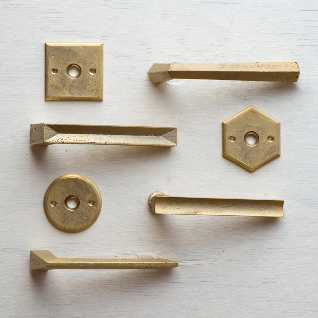 A collection of MATUREWARE Curved Lever brass hardware on a white surface.