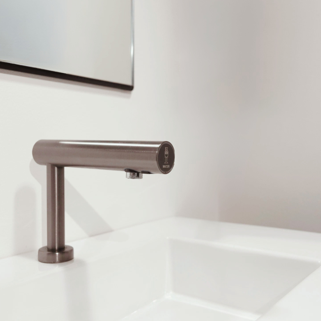 Bathroom sink with a modern deck mounted Dan Dryer stainless steel faucet in a minimalistic setting
