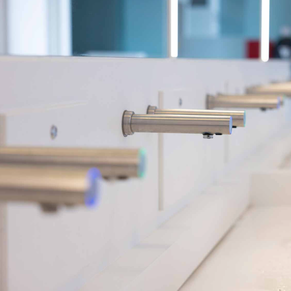Row of modern wall mounted faucets and soap dispensers on a white wall in an airport bathroom