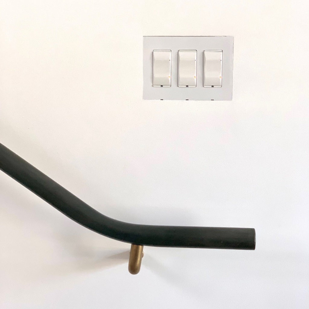 Minimal flush mount wall switch plate above a sleek black handrail with brass brackets.