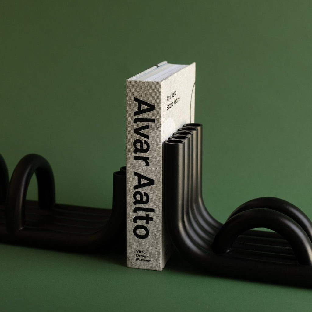 Black TUBE Bookends photographed on a green background with a hard cover Alvar Alto book in between