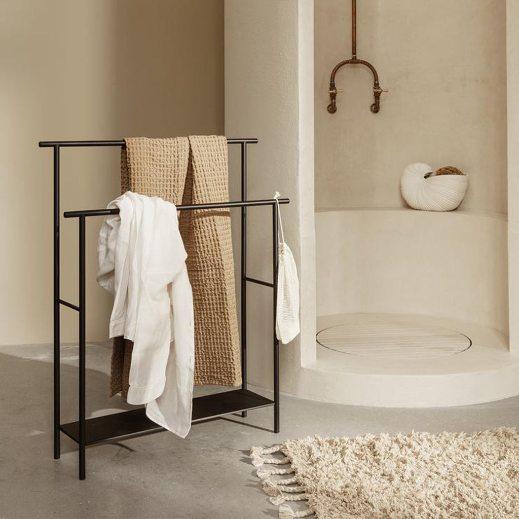 A Ferm Living Dora Towel Stand in a bathroom with a towel on it.