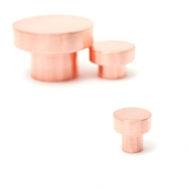 A pair of Baccman Berglund Dot Knobs in pink metal on a white background.
