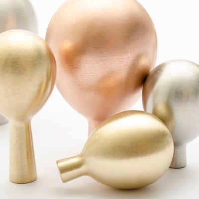 A group of Baccman Berglund Drop Knobs in metallic and gold on a white surface.