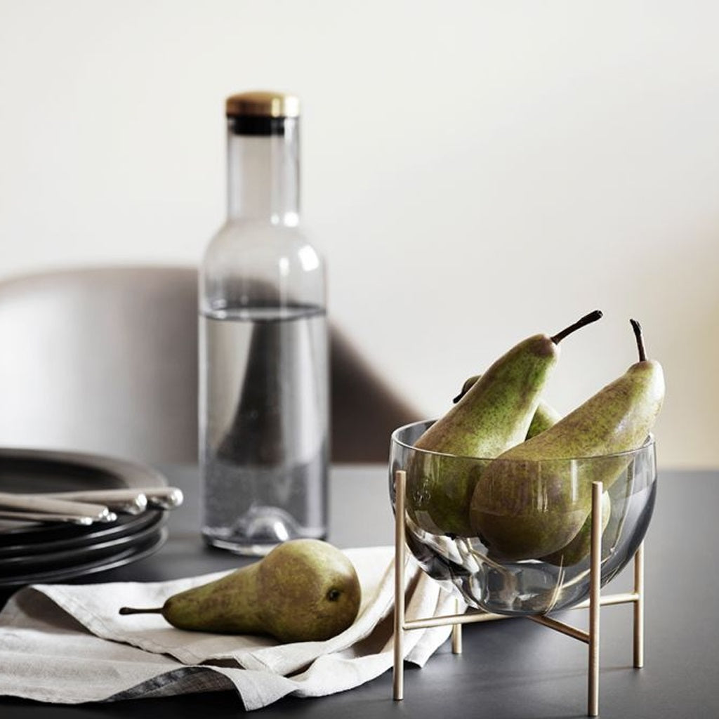 Elegant small bowl filled with pears sitting on a dining table with a modern bottle of water and a table setting..