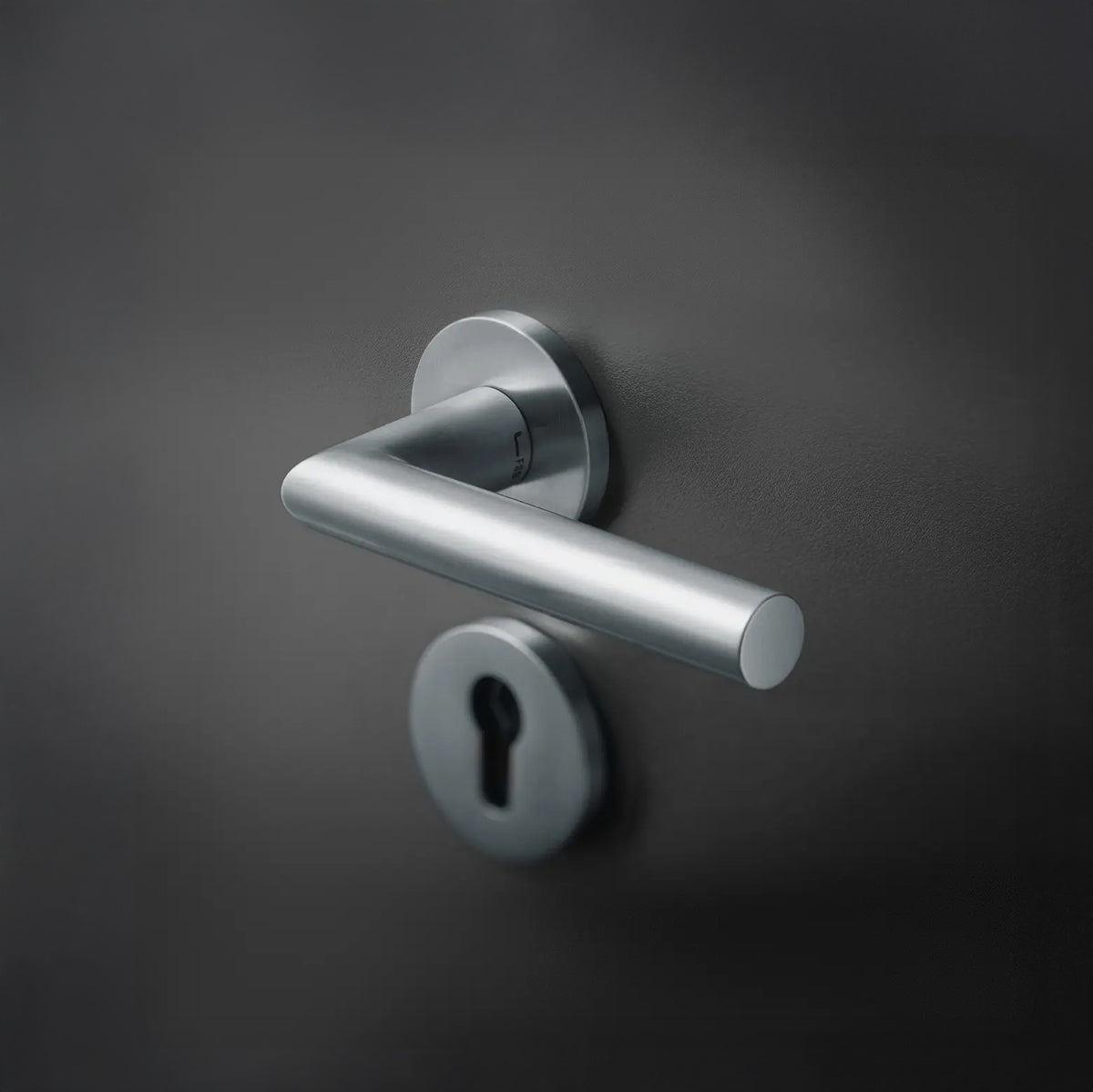 Satin stainless steel FSB 1076 door lever on a dark door with a keyhole escutcheon, showing the mitred square section.